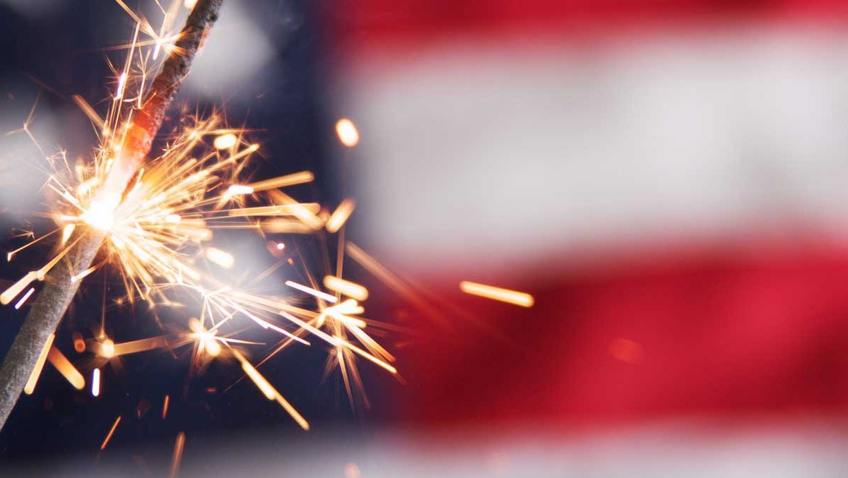 A lit sparkler is in front of an American flag.